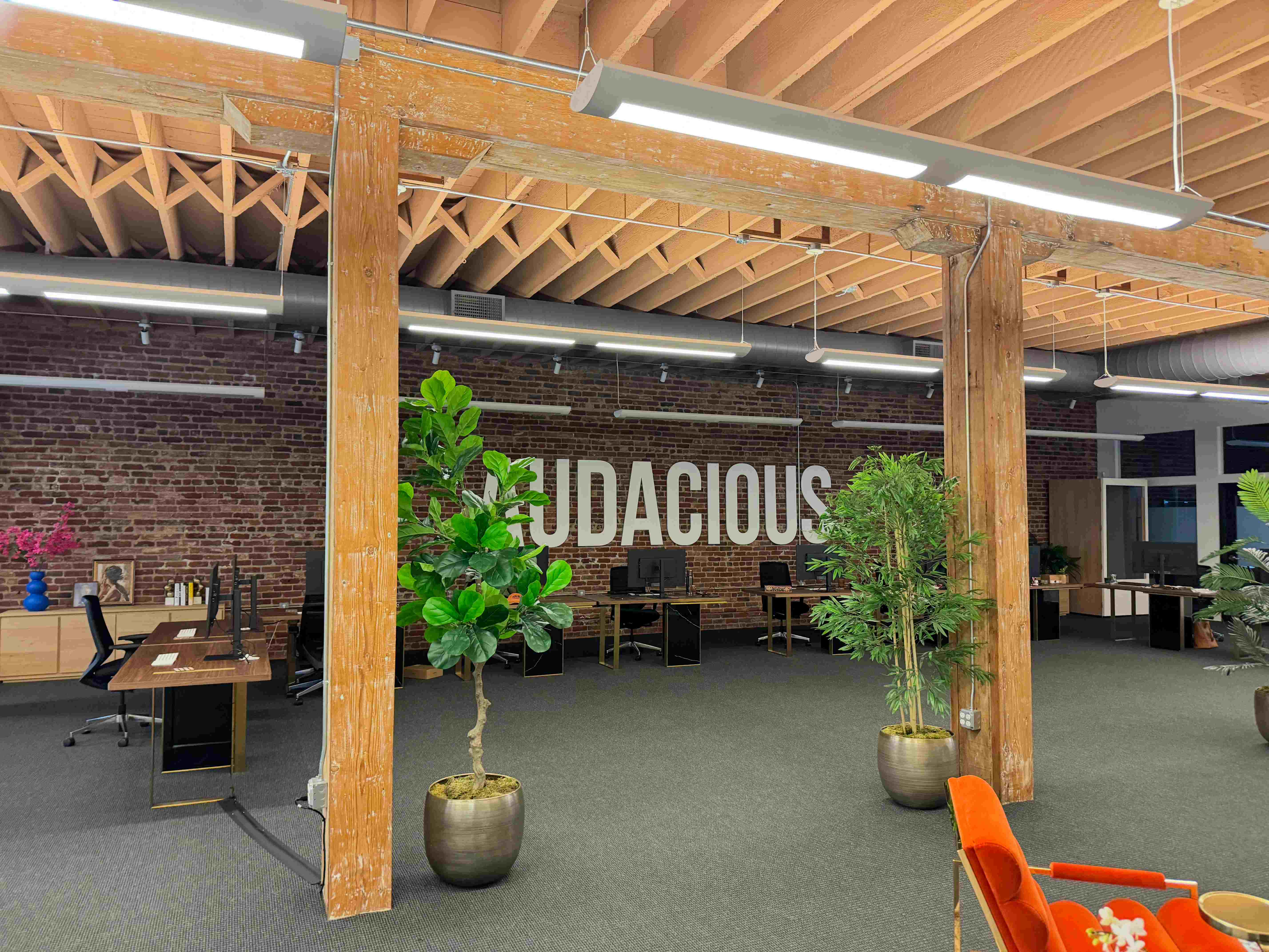 Audacious Ventures office interior with exposed wooden beams, brick wall with company signage, and modern workspace